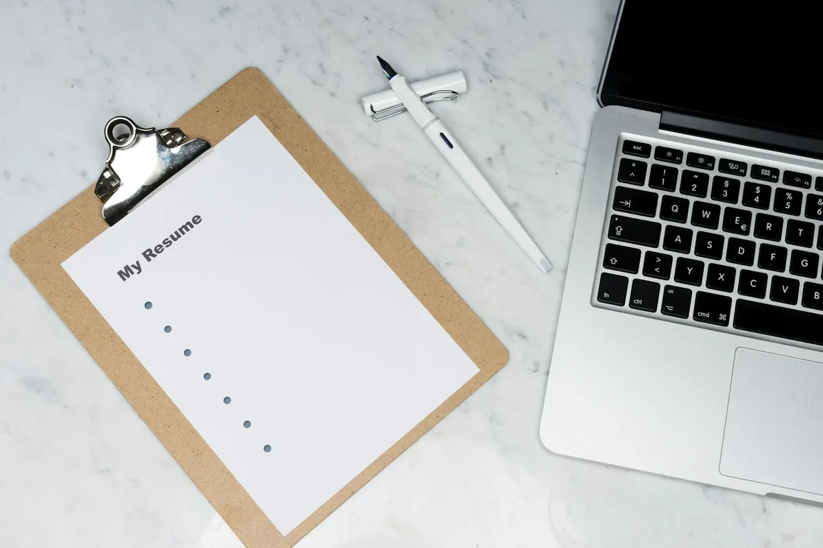A clipboard headed My Resume lying beside an open laptop on a marble desk